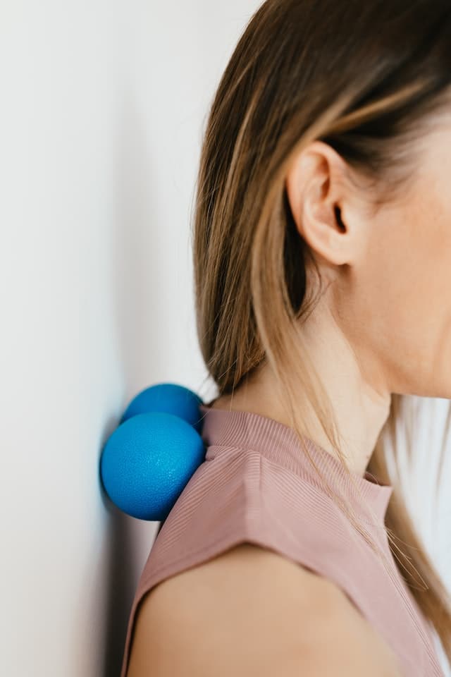 Eine Frau massiert den oberen Nackenbereich mit einem blauen Duo-Faszienball.